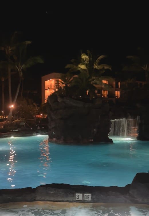 Kōloa Landing main pool waterfall and swim-through grotto lit at night, Poʻipū, Kauai