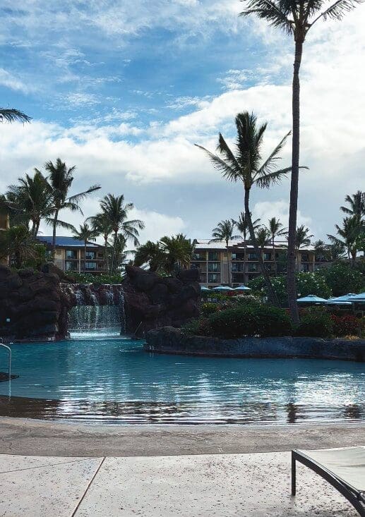Waterfall and swim-through grotto at Kōloa Landing's main pool with villa buildings behind, Poʻipū, Kauai