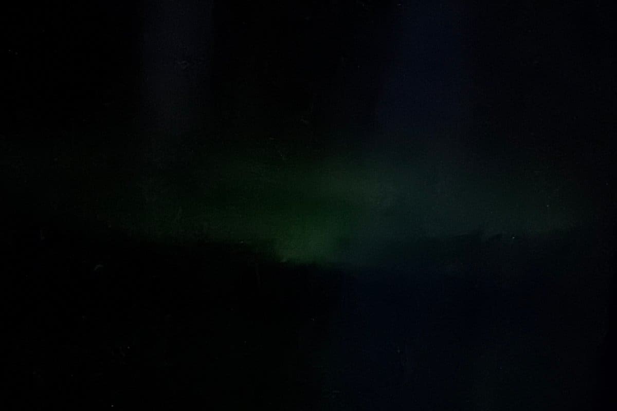 A faint green band of the Northern Lights low over the horizon, seen through an airplane window at night