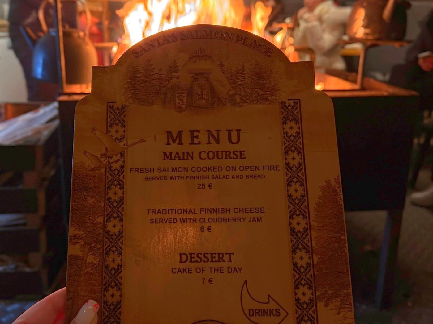 The wooden menu board at Santa’s Salmon Place, held up in front of the open fire where the salmon is cooked
