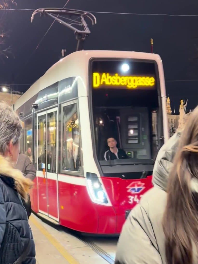 Vienna tram D to Absberggasse pulling into a stop on the Ring at night, people waiting on the platform.