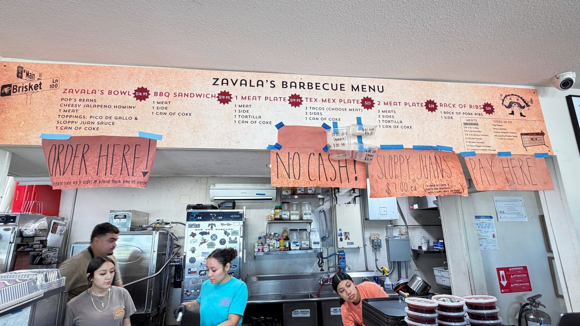 The order counter at Zavala’s Barbecue under a long menu board, with handwritten Order Here, No Cash and Pay Here signs.